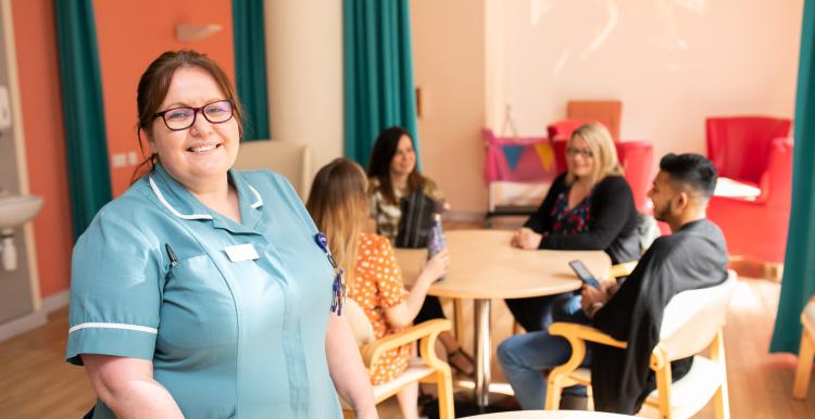 Care worker standing next to table of people sitting.