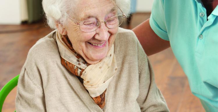 Older woman holding plate of food served by carer.