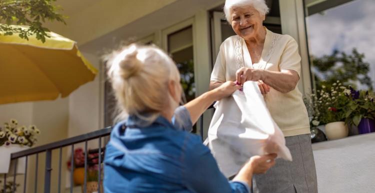 Woman handing a bag of food to an older adult.