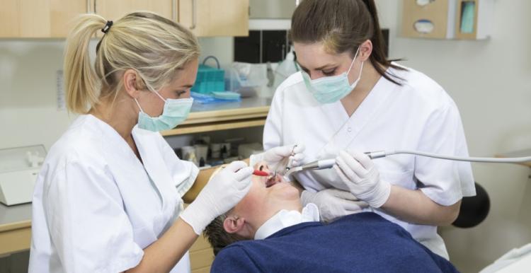 One person receiving treatment from a dentist and dental nurse.