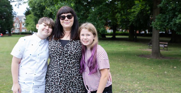 A woman with her arms around two children in a park setting.