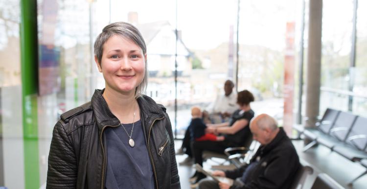 A woman standing in a waiting room smiling at the camera.