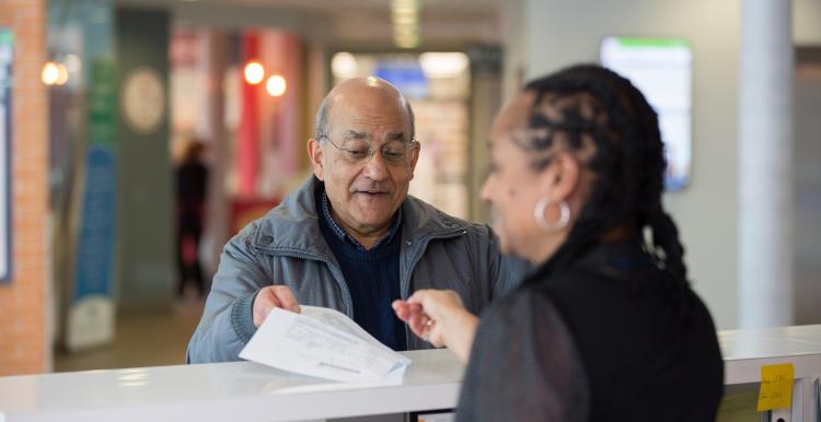 Older man receiving a document from a woman over a counter.