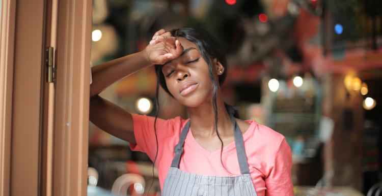 Woman leaning against door frame with arm over her face exhausted