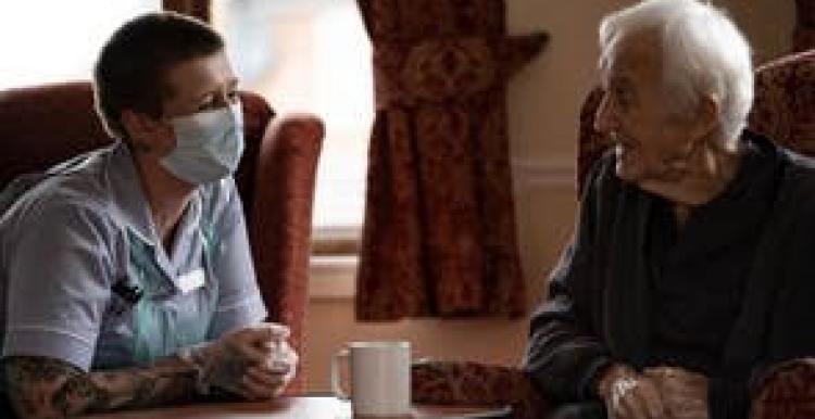 Elderly man and nurse chatting in care home 