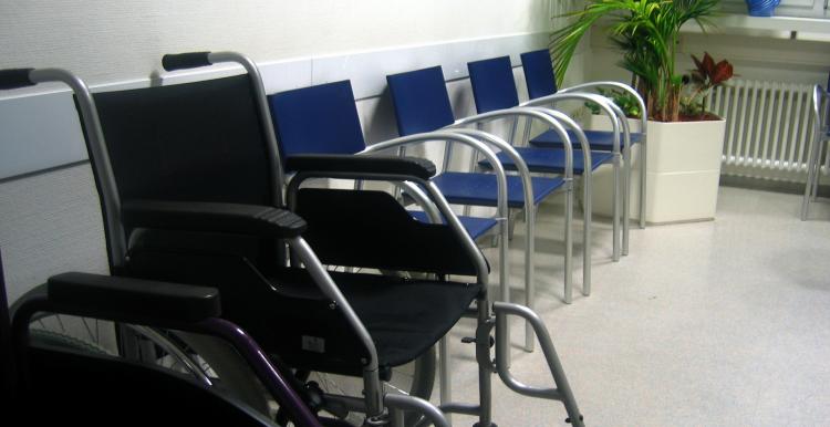 Photograph, wheelchair at front left of image, row of blue chairs alongside