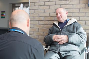 An older man being spoken to by another man.