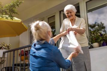 Woman handing a bag of food to an older adult.