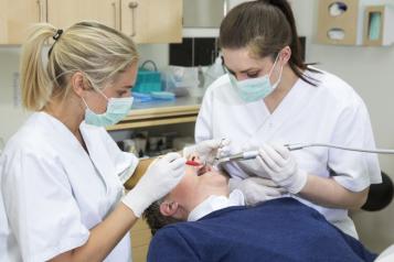 One person receiving treatment from a dentist and dental nurse.