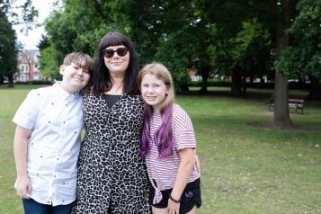 A woman with her arms around two children in a park setting.