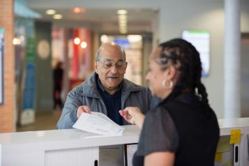 Older man receiving a document from a woman over a counter.