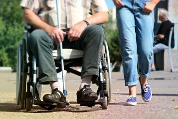 Close up from shoulders down, man in wheelchair to left, someone walking alongside