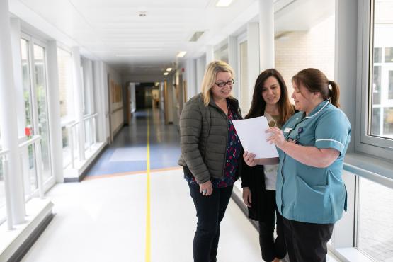 Two women talking to a healthcare professional in a hospital corridor.