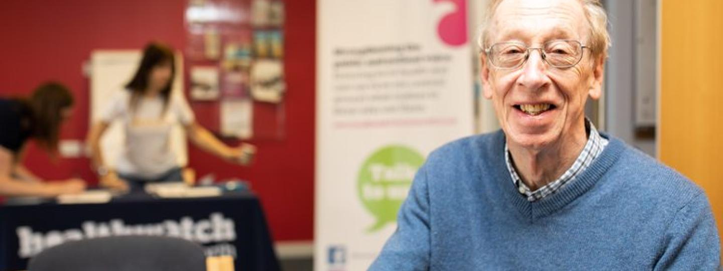 A man smiling with a Healthwatch stall behind him