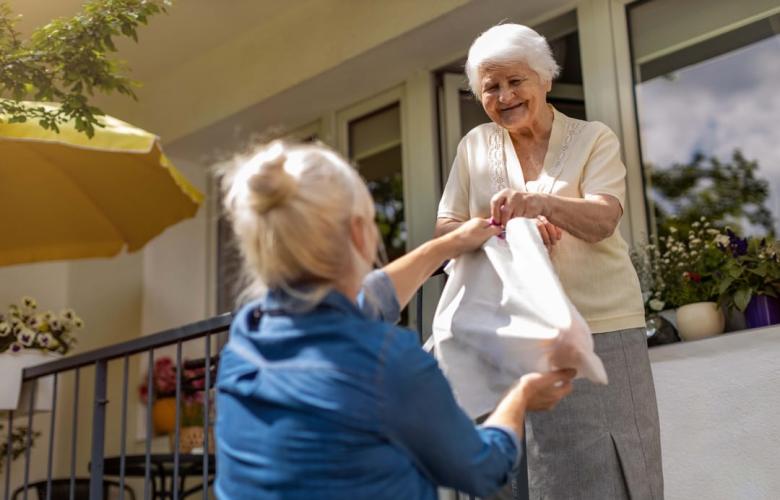 Woman handing a bag of food to an older adult.