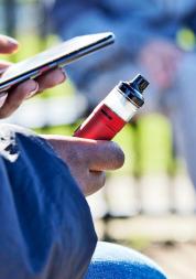 Young person vaping outside with one other young person. 